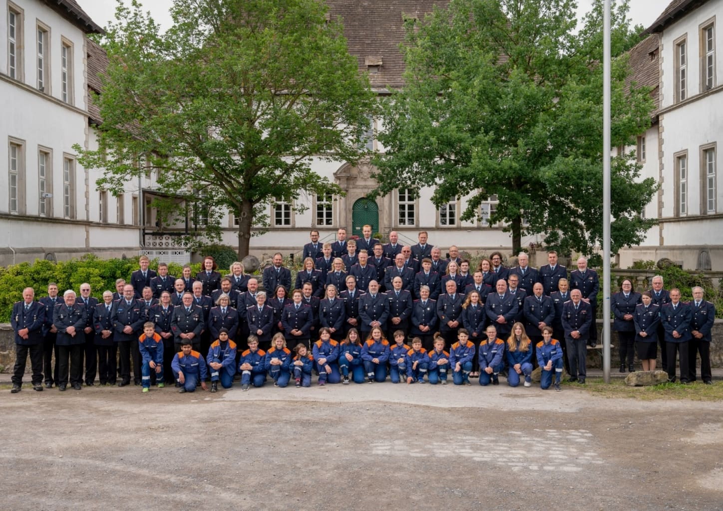 Gruppenfoto der Freiwilligen Feuerwehr Bisperode: Mitglieder in Dienstuniform, davor kniend die Jugendfeuerwehr, vor einem hellen Schlossgebäude